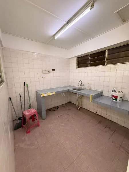 Kitchen features: white tiled walls, grey laminate countertop, single-bowl stainless-steel sink, chrome faucet, window with metal grilles, pink plastic stool, cleaning supplies, floor tiles in beige, fluorescent ceiling lights.