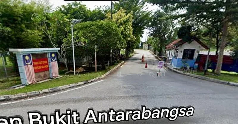 Exterior type: main entrance gate; features: guard house at entrance, paved road, surrounded by greenery, traffic cones, signage, trees lining the road, fenced perimeter; style: modern.