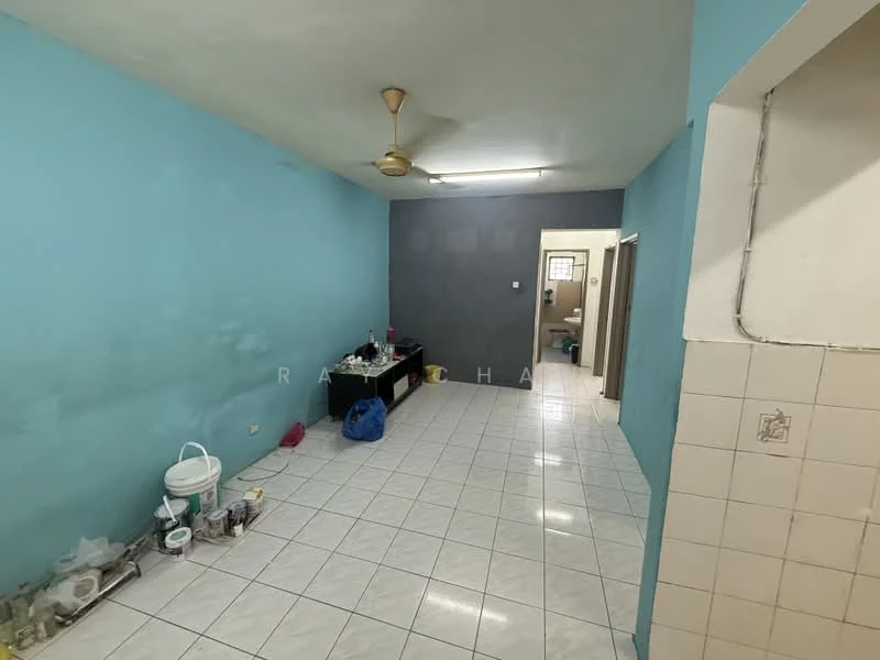Room features: light blue painted walls, grey accent wall, white tiled flooring, ceiling fan, wall-mounted electrical outlet, open space layout, kitchen area visible, various kitchen items on the floor.