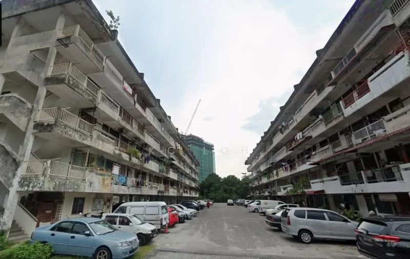 Exterior type: low-rise apartment block; features: two-storey building, balconies with railings, exposed concrete facade, parking lot with multiple vehicles, surrounding greenery, urban context with nearby construction, visible laundry hanging on balconies; style: traditional.