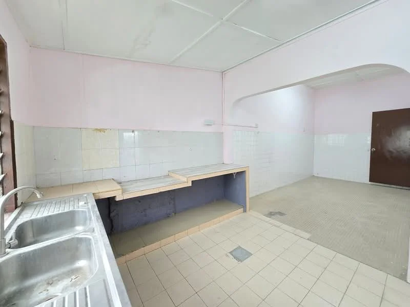 Kitchen features: double-bowl stainless-steel sink, laminate countertop, white tiled backsplash, cream tiled flooring, pink painted walls, exposed wall with grey paint, window with wooden grille, light fixture on ceiling. Room features: cream tiled flooring, white tiled walls, arched doorway, door to another room.