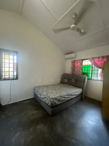 Bedroom features: queen-size bed with floral bedding, upholstered headboard, ceiling fan, wall-mounted air conditioning unit, two windows with metal grills, curtains with floral pattern, concrete flooring, light-colored painted walls.