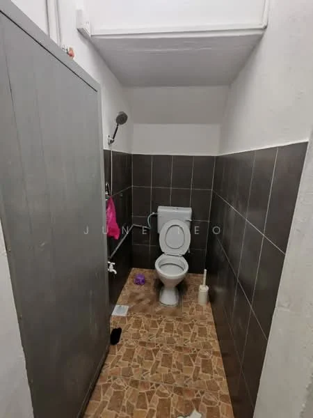 Bathroom features: one-piece toilet, shower with wall-mounted showerhead, grey tiled walls, brown patterned tile flooring, white cistern, toilet brush holder, shower curtain, pink towel hanging, door for privacy.