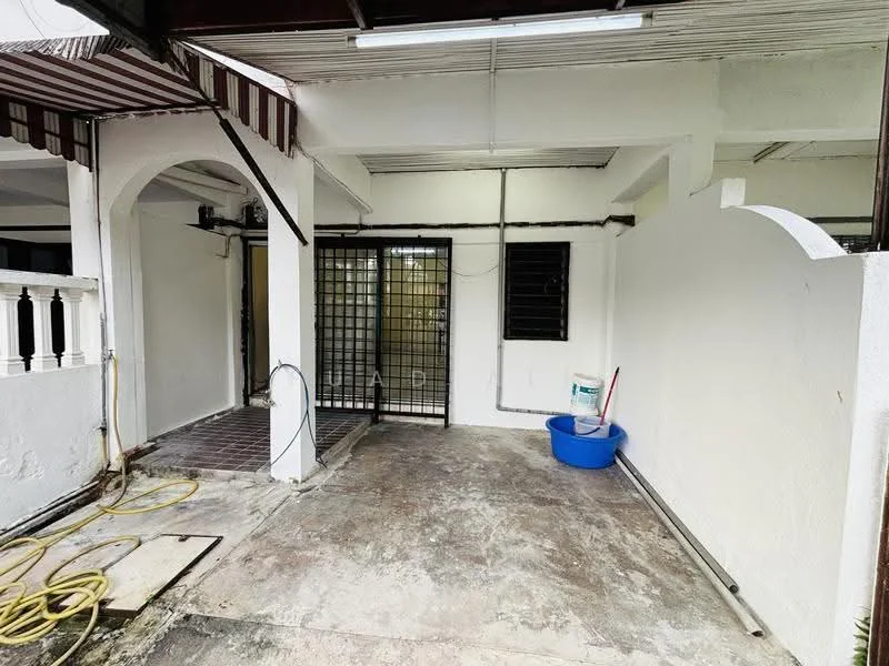 Room features: white painted walls, concrete flooring, metal security grille door, arched entryway, striped awning, blue plastic bucket, exposed electrical wiring, hosepipe on the ground.