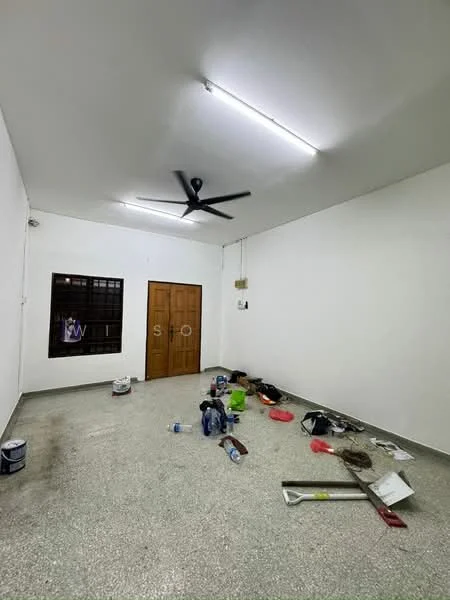 Room features: white painted walls, polished concrete flooring, 5-blade ceiling fan, single wooden door, window with metal grille, various paint cans, cleaning supplies, tools scattered on the floor, fluorescent lighting; style: minimalist.
