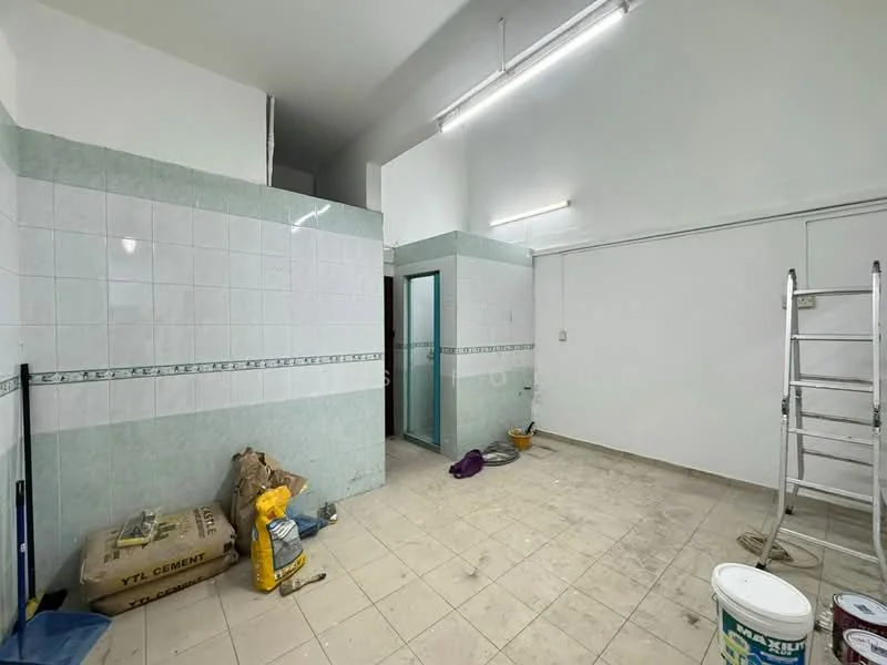 Room features: white tiled walls, light green tiled accents, grey tiled flooring, fluorescent ceiling lights, unfinished space, construction materials on floor, ladder, glass door, plumbing fixtures visible, cement bags, paint bucket.