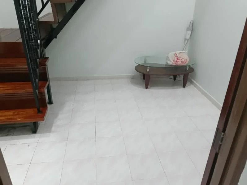 Room features: white painted walls, white tiled flooring, glass coffee table with wooden legs, staircase with wooden steps and black railing, light fixture on wall, empty space, no visible decor.