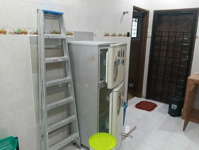Laundry features: white tiled walls, light grey tiled flooring, stainless-steel fridge, step ladder, green plastic bucket, black trash bin, wooden table, metal door, decorative wall tiles with fruit pattern.