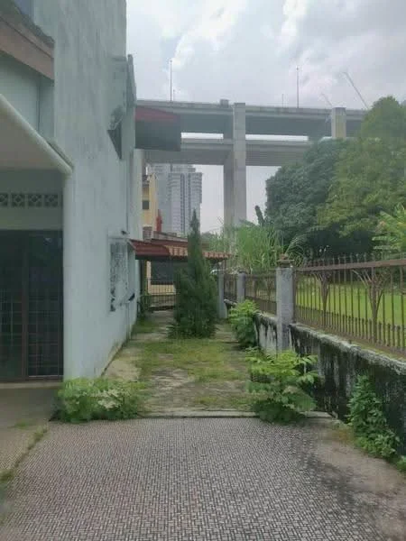 Exterior type: detached bungalow; features: concrete pathway, overgrown vegetation, fenced yard, manicured lawn, surrounding greenery, view of nearby high-rise buildings, proximity to elevated highway, single-storey structure, roof overhang, exterior wall with light blue paint; style: traditional.