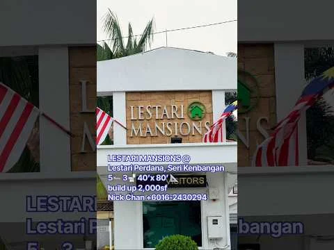 Exterior features: signage with the name 'Lestari Mansions', decorative stone wall, flag poles with Malaysian flags, greenery surrounding the entrance, entrance gate, paved pathway; style: modern.
