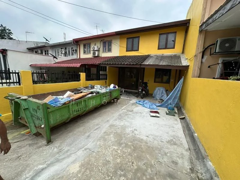 Exterior type: semi-detached house; features: yellow painted facade, metal roof, concrete driveway, green dumpster, exterior air conditioning unit, fenced yard, outdoor storage area, visible motorcycle, partially covered porch; style: modern.