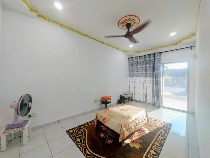 Bedroom features: white painted walls, tile flooring, 5-blade ceiling fan, sliding glass door, sheer curtains, decorative ceiling rose, area rug with floral pattern, bed with decorative bedspread, small side table, standing fan.