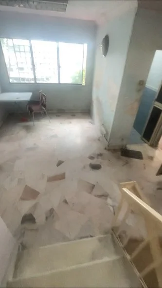 Room features: marble flooring, light blue painted walls, large windows, staircase, ceiling light fixture, table with chairs, visible wall damage, no visible appliances or furniture.