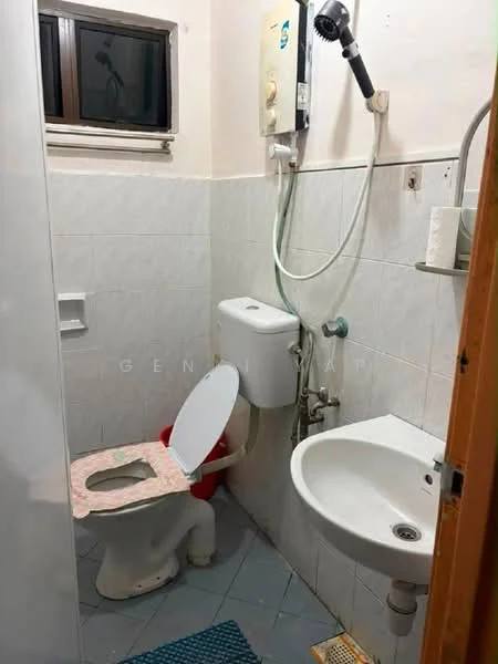 Bathroom features: white tiled walls, grey tiled flooring, one-piece toilet, sink with chrome faucet, shower with handheld showerhead, window for natural light, toilet paper holder, red plastic toilet seat, shower water heater, small mirror above sink.