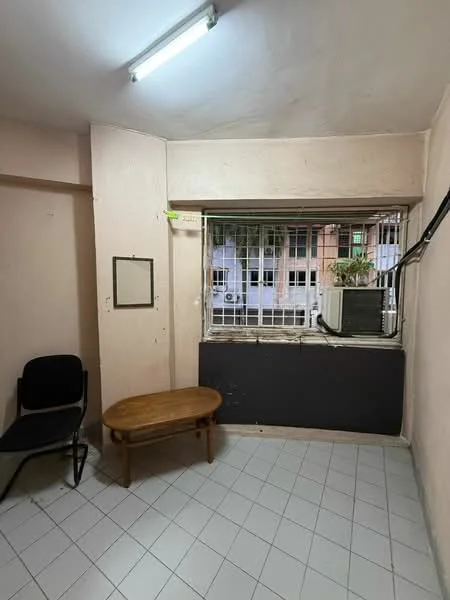 Room features: light grey painted walls, white ceiling, tile flooring, single window with security bars, air conditioning unit, wooden coffee table, black chair, corner space, exposed electrical wiring.