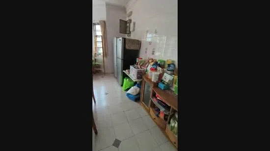 Kitchen features: white tiled walls, white tiled flooring, black fridge, wooden shelving unit, various kitchen items on shelves, window with sheer curtains, green plants, dining table, multiple bags and containers.