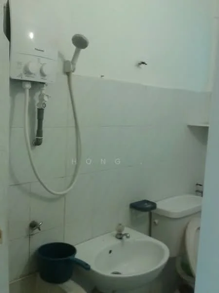 Bathroom features: white tiled walls, white tiled flooring, shower head with hose, toilet, sink with faucet, blue bucket, wall-mounted mirror, shelf above sink.