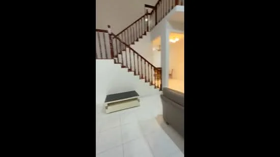 Room features: white painted walls, white tiled flooring, wooden staircase with railing, recessed lighting, open layout, neutral color palette, sofa, coffee table; style: modern.