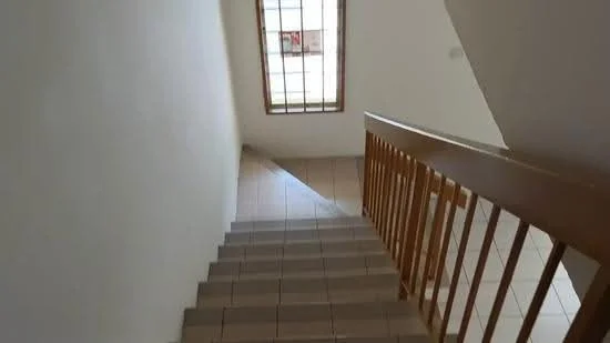 Room features: tiled flooring, white painted walls, wooden handrail, window with security bars, staircase, natural light from window.