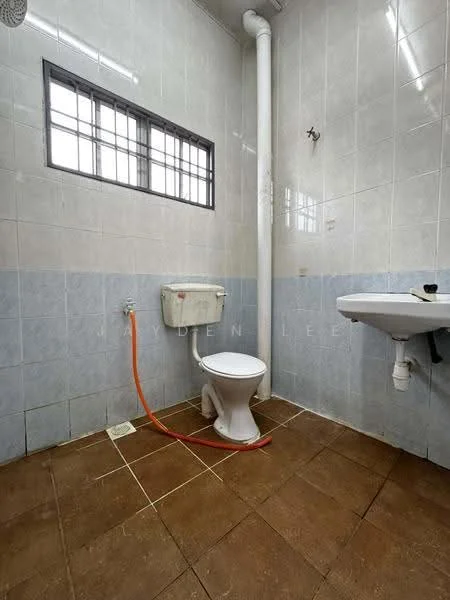 Bathroom features: white tiled walls, light blue tiled walls, brown ceramic tile flooring, one-piece toilet, wall-mounted toilet tank, sink with wall-mounted faucet, small window, exposed plumbing, orange water supply line.