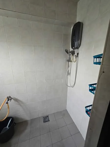 Bathroom features: white tiled walls, grey tiled flooring, shower area with wall-mounted showerhead, handheld shower, water heater unit, plastic storage baskets, drainage grate, bucket for water.
