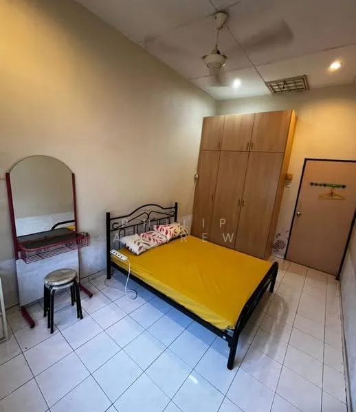Bedroom features: queen-size bed with yellow bedding, black metal bed frame, wooden wardrobe with sliding doors, white tiled flooring, ceiling fan, wall-mounted mirror, small wooden stool, decorative pillows, light-colored walls, door to hallway.