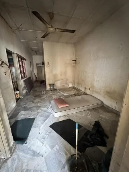 Room features: marble flooring, white painted walls, ceiling fan, mattress on the floor, window with wooden frame, exposed electrical outlets, wall-mounted electrical panel, cleaning tools visible.