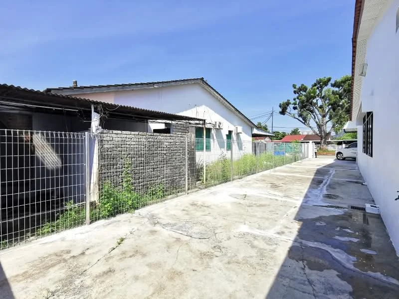 Exterior type: linked terrace house; features: concrete driveway, fenced perimeter, single-storey buildings, manicured grass patches, exposed concrete surface, surrounding greenery, car parked in driveway; style: traditional.