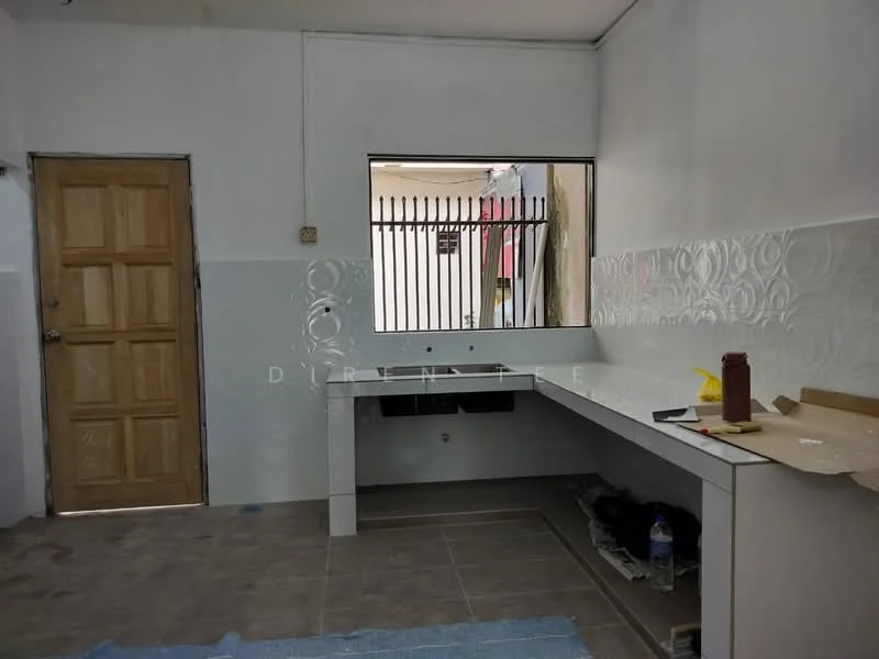 Kitchen features: white painted walls, grey tiled flooring, single-bowl sink, countertop with backsplash, wooden door, window with metal grille, unfinished cabinetry, water bottle on floor, blue mat on floor.