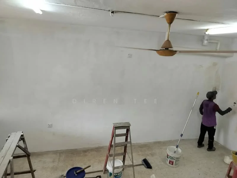 Room features: white painted walls, ceiling fan, concrete flooring, ladder, paint bucket, paint roller, person painting wall, light fixtures.