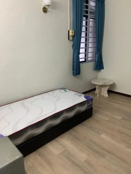 Bedroom features: single bed with mattress, light wood laminate flooring, white painted walls, curtains in teal, window with metal grille, small round table, wall-mounted light fixture.