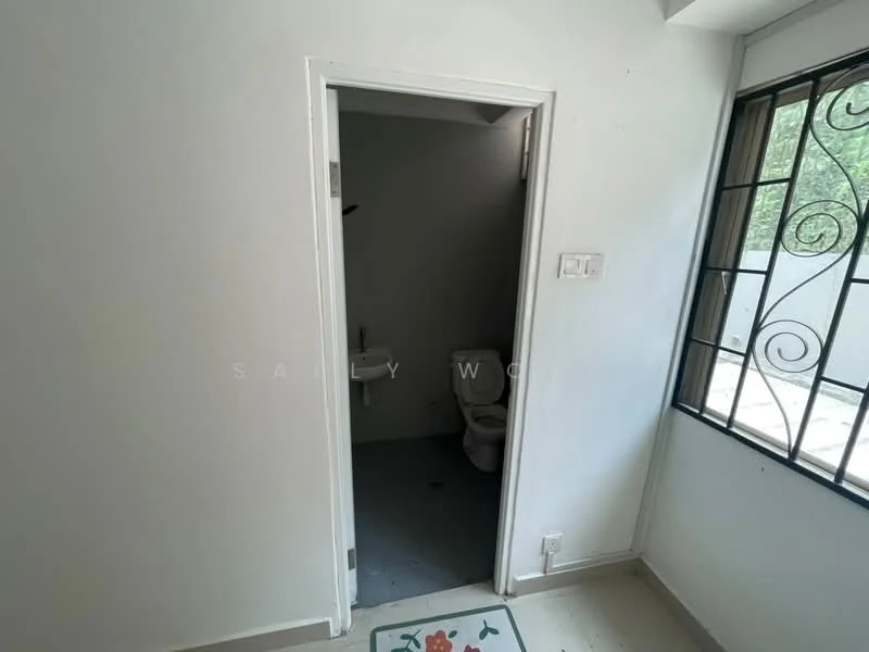 Room features: white painted walls, grey tiled flooring, window with metal grille, door leading to bathroom, visible toilet in bathroom, natural light from window.