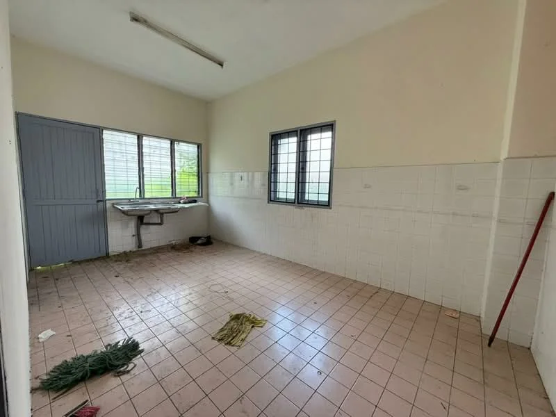 Room features: white tiled walls, light beige tiled flooring, single-bowl sink, window with metal grille, two large windows, plain ceiling, cleaning broom, mop, visible dirt on floor.