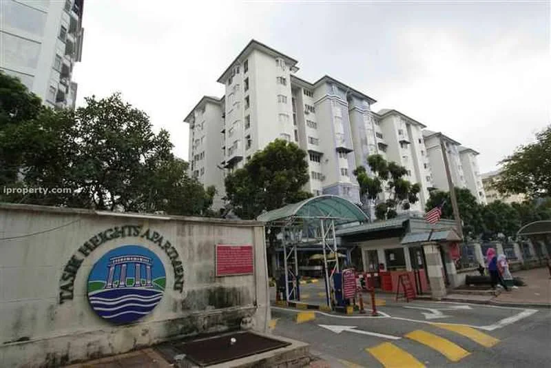 Exterior type: low-rise apartment block; features: white painted facade, 5-storey building, entrance gate with security booth, landscaped garden with trees, paved driveway, signage with building name, visible parking area, surrounded by greenery; style: modern.
