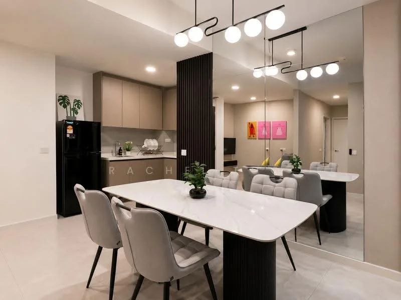 Dining features: rectangular dining table with marble top, 4 upholstered dining chairs in light grey, pendant lighting with round bulbs, mirrored wall, kitchen cabinetry in light beige, black refrigerator, potted plants on table, wall-mounted TV, artwork with pink frames, light grey tiled flooring; style: modern. Kitchen features: kitchen cabinetry in light beige, stainless-steel sink, chrome faucet, built-in oven, cooktop, black refrigerator; style: modern.