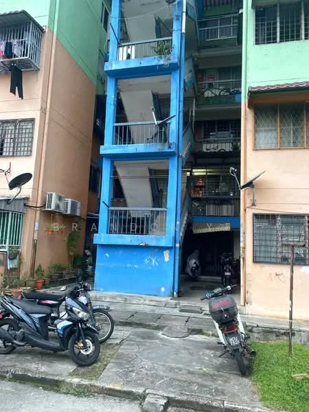 Exterior type: low-rise apartment block; features: blue painted facade, orange painted facade, exposed concrete structure, balconies with metal railings, staircase with metal railing, visible air conditioning units, multiple satellite dishes, parking area with motorcycles, ground-level entrance, windows with metal grilles; style: modern.