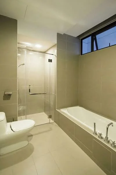 Bathroom features: white one-piece toilet, walk-in shower with glass enclosure, rain shower head, built-in bathtub, chrome basin mixer for bathtub, chrome basin mixer for shower, grey tiled walls, light grey tiled flooring, recessed downlights, window for natural light; style: modern.