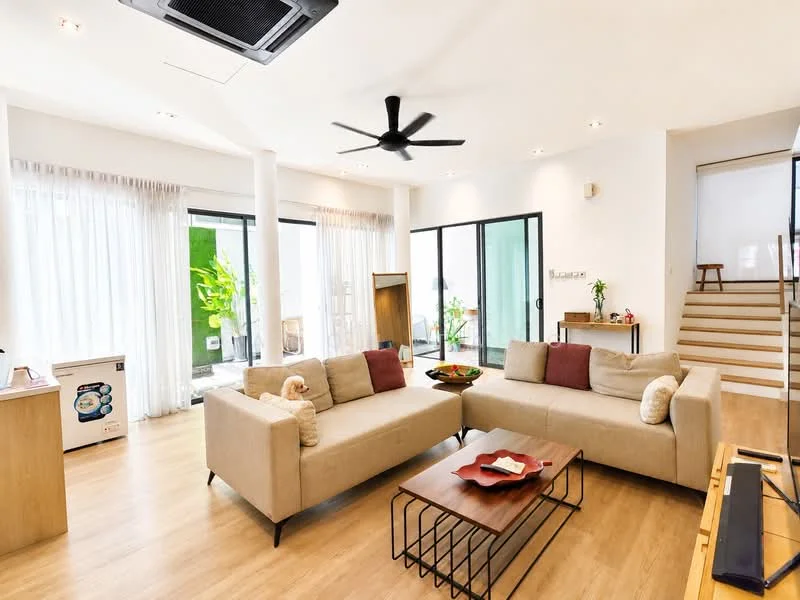Living features: 3-seater fabric sofa in beige, 2-seater fabric sofa in beige, coffee table with geometric design, TV console, wall-mounted TV, ceiling fan with light, floor-to-ceiling windows, sheer curtains, wooden flooring, decorative plants, open layout, staircase in background; style: modern; view: garden.