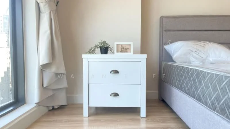 Bedroom features: queen-size bed, upholstered headboard, white bedside table with two drawers, decorative photo frame, small potted plant, floor-to-ceiling window, curtains, laminate flooring, neutral wall color; style: modern.