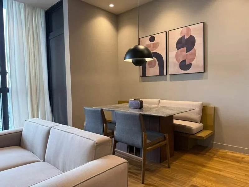 Dining features: wood dining table with marble top, upholstered bench seating, 4 dining chairs, pendant lamp, framed abstract artwork on walls, light brown wooden flooring, floor-to-ceiling windows with sheer curtains; style: modern; view: city. Living features: 3-seater fabric sofa in light grey, light brown wooden flooring; style: modern.