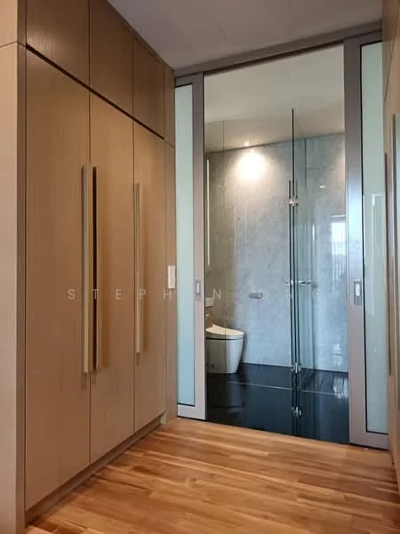 Room features: wooden flooring, built-in cabinets with light wood finish, glass door leading to bathroom, marble wall in bathroom, black tile flooring in bathroom, toilet visible through glass door, modern hardware on cabinets; style: modern.