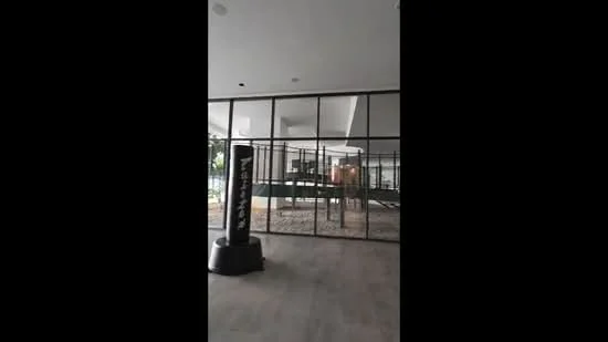 Room features: large glass windows, concrete flooring, modern lighting fixtures, open layout, indoor greenery, gym equipment visible, high ceiling, neutral wall color; style: modern; view: garden.