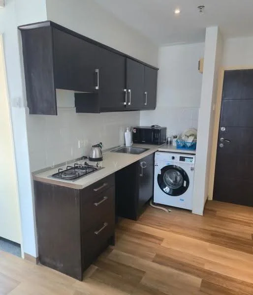 Kitchen features: dark wood cabinetry, light-colored countertop, stainless-steel gas hob, stainless-steel kettle, microwave, front-load washing machine, single-bowl stainless-steel sink, chrome pull-down faucet, tile backsplash, wooden flooring, recessed downlights; style: modern.