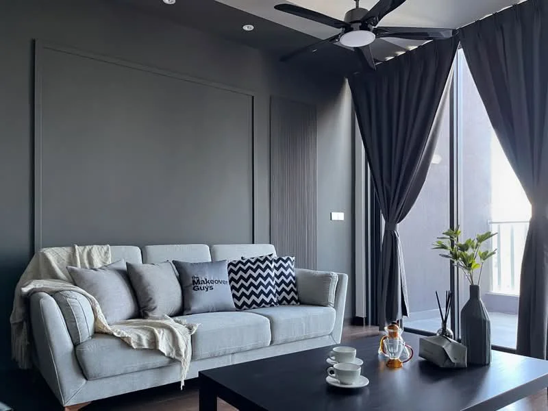 Living features: 3-seater fabric sofa in grey, decorative cushions with various patterns, dark accent wall, recessed ceiling lights, 5-blade ceiling fan with light, floor-to-ceiling windows, blackout curtains, wooden flooring, coffee table, decorative vase with flowers, decorative items on the table; style: modern.