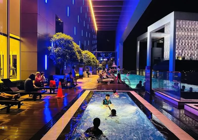 Exterior type: swimming pool deck; features: infinity pool, lap pool, pool deck with loungers, landscaped area with trees, ambient lighting, water features, seating areas, safety cones, nighttime setting; style: modern.