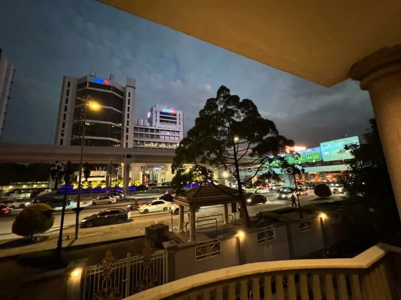 Exterior features: city skyline, street view, traffic on main road, commercial buildings, overhead train track, trees in foreground, street lighting, nighttime setting; style: modern.