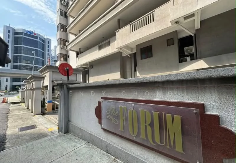 Exterior type: low-rise apartment block; features: cream painted facade, signage with 'The Forum', surrounding urban context, visible air conditioning units, paved walkway, adjacent road, nearby commercial buildings; style: modern.