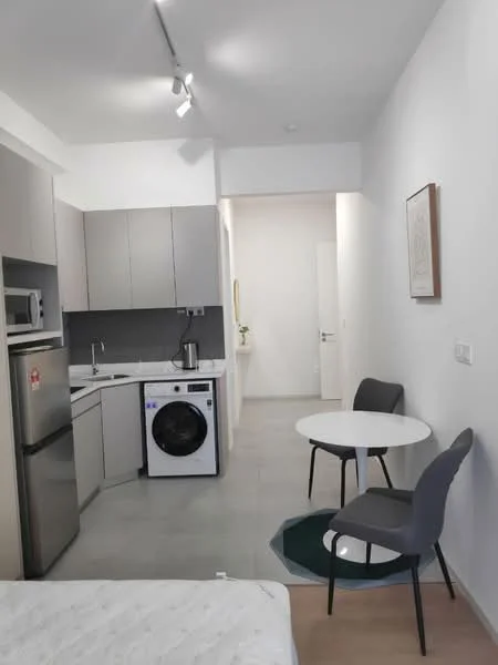 Kitchen features: grey cabinetry, white countertops, stainless-steel fridge, built-in oven, 4-burner gas hob, single-bowl stainless-steel sink, chrome pull-down faucet, white washing machine, tile backsplash, recessed downlights, floor-to-ceiling cabinets, open shelving, dining table for two, grey dining chairs; style: modern. Room features: light-colored flooring, white painted walls, doorway leading to hallway.