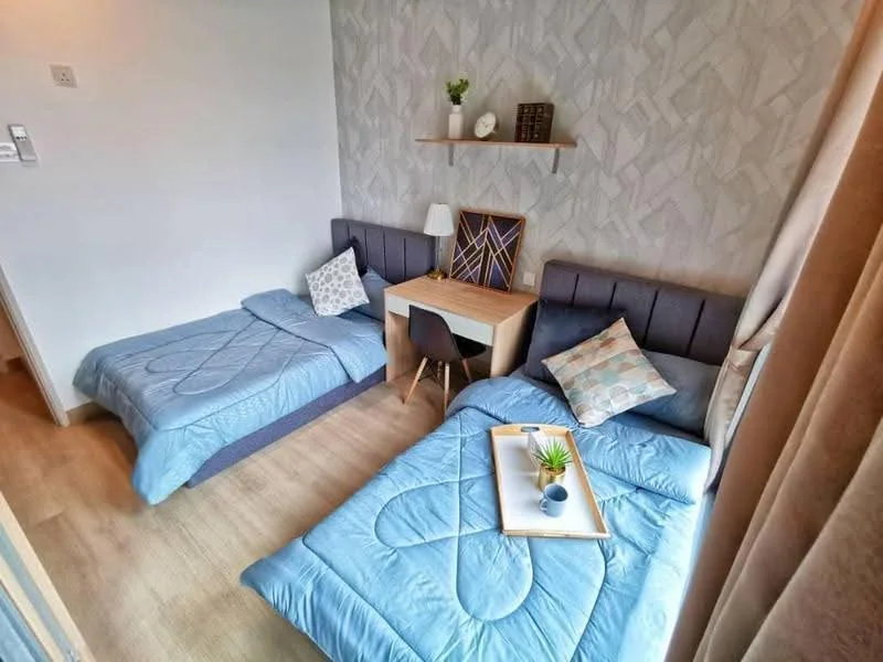 Bedroom features: two single beds with blue bedding, wooden flooring, geometric patterned wallpaper, shelf above the desk, study desk with chair, table lamp, decorative artwork, decorative pillow on bed, small potted plant on desk; style: modern.