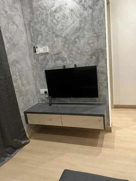 Room features: grey textured wall, light wood flooring, wall-mounted TV, floating TV console with drawers, remote control on console; style: modern.